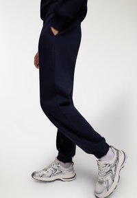 Granatowe spodnie dresowe z bocznymi kieszeniami, zwężanymi nogawkami i ściągaczami, zestawione z srebrnymi sneakersami z siateczkową cholewką i masywną podeszwą.
