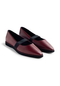 Une paire de ballerines en cuir rouge foncé avec des pointes et des sangles élastiques noires sur le dessus, sur un fond blanc.