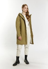 Olivegrøn polstret parka med hætte, der har en frontlynlås, sidelommer og en blød indvendig foring. Sæt sammen med off-white bukser og sorte støvler.