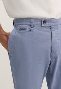 Hellblaue, strukturierte Hose mit geradem Schnitt, ausgestattet mit einem Knopfverschluss, seitlichen Taschen und einem hinteren Taschendetail.