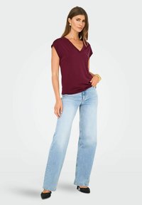 Top burdeos de cuello en V con mangas cortas, combinado con jeans de pierna ancha en azul claro y zapatos negros de punta. Tejido suave, corte relajado.