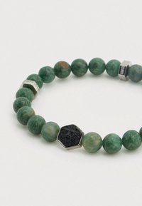 Βραχιόλι με πράσινη πολύτιμη πέτρα που διαθέτει στρογγυλά χάντρες, εξάγωνη μαύρη διακόσμηση λέοντα και ασημένια εξαρτήματα με χαραγμένες λεπτομέρειες.