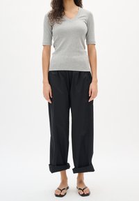 Grå ribbad T-shirt med korta ärmar och V-ringning, kombinerad med löst sittande svarta byxor, uppvikta fållar och svarta platta sandaler. Enkelt, vardagligt klädval.