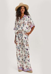 Lehké dvoudílné oblečení s květinovým vzorem, zahrnující volnou košili a široké kalhoty; barvy zahrnují krémovou, modrou a fialové akcenty.