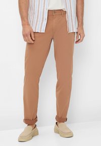 Tan chino's gemaakt van lichtgewicht stof, met een slanke pasvorm, opgerolde mouwen en een klassieke knoopsluiting, gecombineerd met beige instappers.