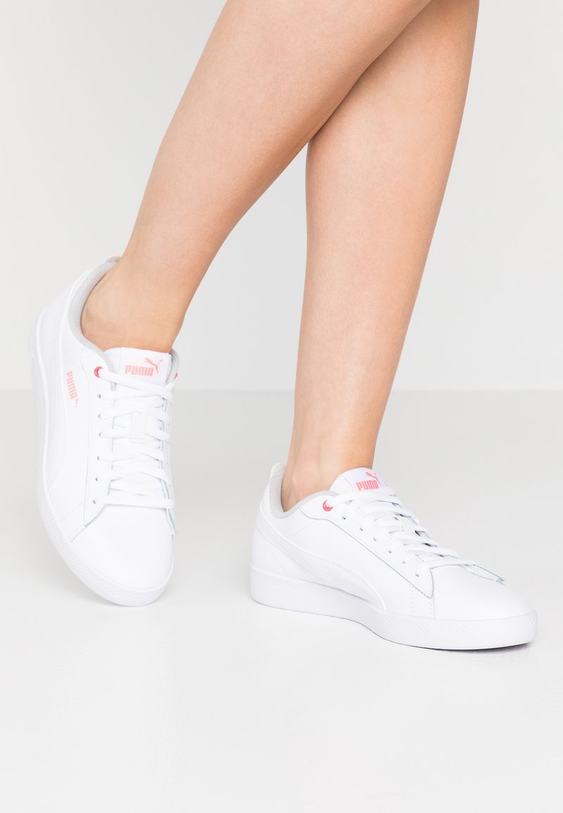 Zapatillas blancas hechas de material sintético liso con detalles en rosa en el logo y los ojales, con un diseño de corte bajo y suela de goma plana.