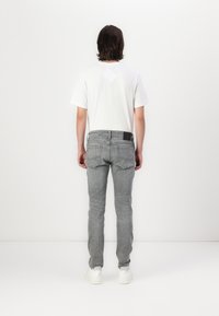 Tenue pour homme avec un t-shirt blanc et un jean en denim gris. Les jeans ont une coupe slim, avec une étiquette noire à la taille et aux poches arrière.