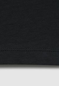 Lähikuva mustasta kankaasta, jossa yksityiskohtainen vaakasuora ommel lähellä ala-reunaa vaaleanharmaalla taustalla.