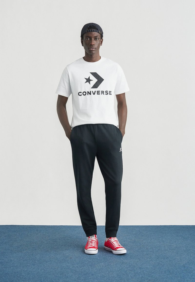 Herreoutfit med en hvid bomuld t-shirt med sort "Converse"-logo, sorte joggebukser og røde sneakers med hvide såler.