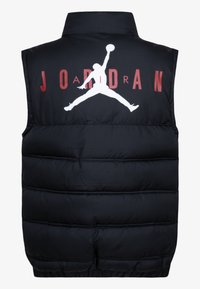 Chaleco acolchado negro con un cuello alto, que presenta un gran logo Jumpman blanco y "JORDAN" en texto rojo en la parte posterior. Textura de tela suave.