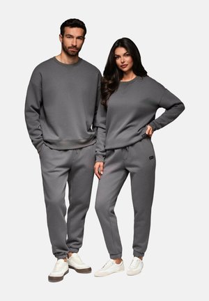 Zwei Modelle tragen passende graue Sweatshirts und Sweatpants aus weichem Stoff. Die Sweatpants haben elastische Bündchen und einen elastischen Bund.