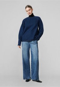 Felpa in denim blu scuro con scollatura rotonda e vestibilità rilassata. Abbinata a jeans a gamba larga blu chiaro e scarpe nere a punta.
