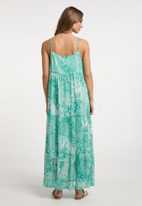 Rochie maxi verde cu flori, cu bretele tip spaghetti, design cu straturi, țesătură ușoară și textură translucidă, prezentând modele paisley.