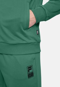 Conjunto de sudadera y pantalones verde, de mezcla de algodón, que incluye un bolsillo frontal, puños acanalados y detalles del logo negro en los pantalones.