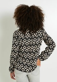 Blusa negra y beis con estampado, con dobladillo redondeado, mangas largas y un corte relajado. Presenta grandes formas abstractas y un detalle en el hombro trasero.