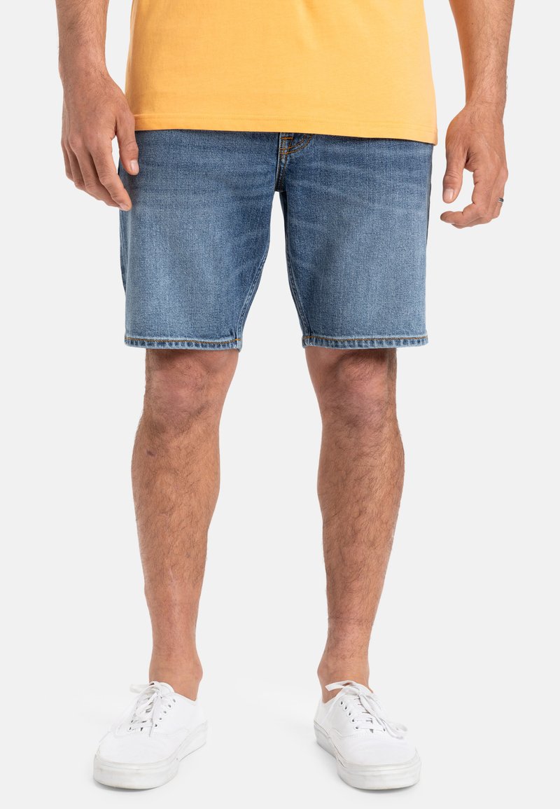 Shorts de denim en azul claro, con un corte recto, dobladillo deshilachado y un ajuste casual. Combinados con zapatillas blancas de cordones.