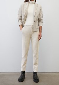 Blazer beige texturé avec un pantalon tapered assorti, associé à un col roulé blanc et des bottes à talons épais noires. Accents de boutons simples.