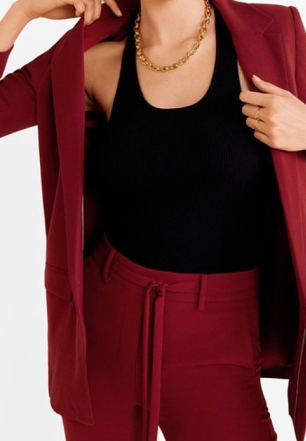 Blazer bourgogne sur un débardeur noir à côtes, associé à un pantalon taille haute assorti. Comprend un collier en chaîne dorée et un détail de taille noué.