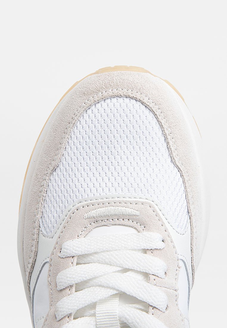 Baskets avec une tige en maille blanche, des accents en suède gris clair, des lacets crème et une semelle en caoutchouc texturé. Présente un design à bout arrondi.