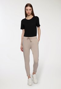Czarna koszulka z krótkim rękawem zestawiona z beżowymi spodniami dresowymi z elastycznym pasem i sznurkiem. Białe trampki dopełniają całość.