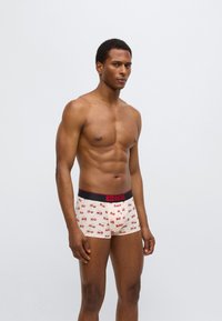 Ανδρικό βαμβακερό εσώρουχο τύπου trunk με ανοιχτό μπεζ φόντο και επαναλαμβανόμενο μοτίβο με κεράσια, μαύρη ζώνη μέσης με το λογότυπο Diesel και εφαρμοστό σχέδιο.