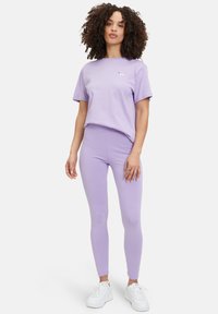 T-shirt di cotone lilla e leggings abbinati, entrambi attillati. Il T-shirt presenta un piccolo logo, mentre i leggings hanno una texture liscia. Abbinati a sneaker bianche.