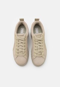 Sneaker beige in suede con punta arrotondata, sistema di allacciatura con sei occhielli e collare imbottito; presenta un logo sulla linguetta e dettagli laterali.