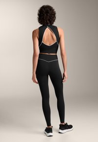 Musta urheilullinen crop-top, jossa on takana leikkaus ja valkoinen reunus, yhdistettynä mustiin korkeavyötäröisiin legginsseihin, joissa on sileä pinta.