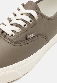 Gros plan sur une chaussure Vans en cuir marron avec des lacets blancs et une épaisse semelle en caoutchouc blanche sur un fond clair.