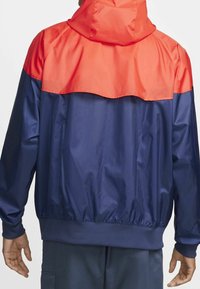 Blue and red windbreaker with a hood, featuring a smooth, shiny texture and elastic cuffs. Contrast color at the shoulders and waist.