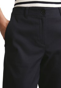 Pantalon bleu marine en tissu résistant, avec devant plat, poches latérales et fermeture à bouton unique à la taille.
