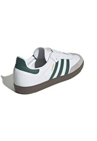 Vita lädersneakers med gröna ränder, grå mockatå spänne och brun gummisula. "Samba"-logotyp i guld på sidan.