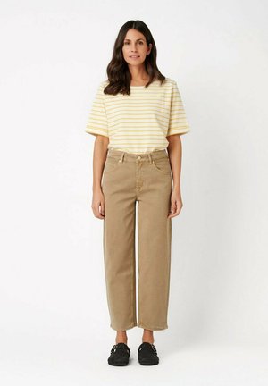 Woman with long dark hair wearing a yellow and white striped short-sleeve shirt, beige high-waisted pants, and black slip-on shoes.