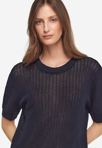 Mörkblått stickat tröja med en lös, strukturerad design, korta ärmar och rundad nacke med subtila öppna stickdetaljer.