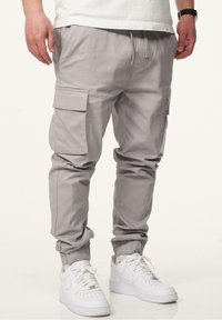 Hellegraue Cargo-Hosen mit schmaler Passform, elastischen Bündchen und mehreren Seitentaschen, kombiniert mit weißen Sneakers.