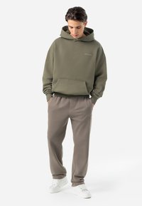 Hanorac verde măsliniu cu buzunar frontal, asortat cu pantaloni confortabili de culoare bej deschis. Adidași albi completează ținuta. Un look casual și lejer.