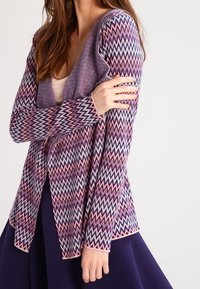 Wielokolorowy sweter na drutach z wzorem zygzaków w kolorach różowym, fioletowym i kremowym, z długimi rękawami i otwartym przodem.