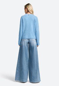 Light blue fuzzy sweater with long sleeves, round neckline, and a small back logo. Paired with oversized light blue denim wide-leg pants.