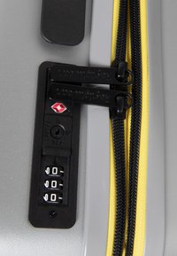 Valigia grigia con zip gialla e nera, dotata di lucchetto a combinazione, superficie testurizzata e logo del marchio Regulator sul meccanismo del lucchetto.