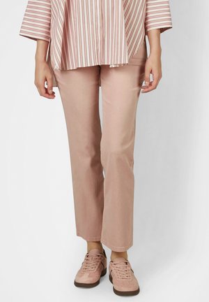 Person wearing light pink straight-leg pants, matching pink lace-up sneakers, and a loose striped shirt with long sleeves.