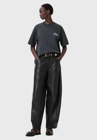 Mustat leveälahkeiset nahkahousut yhdistettynä tummanharmaaseen t-paitaan, jossa pieni kuvio. Malli käyttää kultakoristeista vyötä ja liukuvia kenkiä.