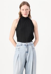 Zwarte geplooide halter bodysuit met een hoge hals en open rug, gecombineerd met lichtblauwe loose-fit spijkerbroek met geplooide details.