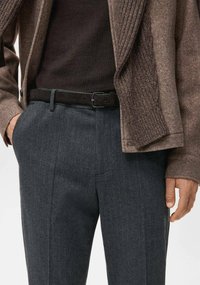 Brązowa teksturowana kurtka na ciemnej koszuli, zestawiona z szarymi spodniami w prążki i czarnym paskiem. Strój wykonany jest z gładkich, strukturalnych tkanin.