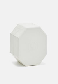 Pain de savon blanc octogonal avec logo embossé centré sur un fond blanc uni.