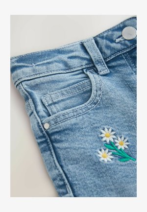 Sinised teksapüksid tikitud lillekujundusega, millel on valged mummulilled ja rohelised lehed. Sisaldab esitaskut ja metallist nööbi kinnitust.