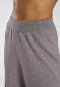 Grå stickade byxor med ribbad midja, med en mjuk textur och avslappnad passform, visade från sidan för att framhäva midjedetaljen.