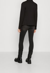 Svart blazer med långa ärmar, parat med mörkgrå skinny jeans och kraftiga svarta ankelstövlar. Enkelt design, slät textur.