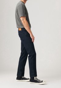 Jeans de mezclilla azul oscuro con corte recto, que se llevan con una camiseta de cuello redondo gris y zapatillas altas negras. Etiqueta de cuero en la cinturilla.