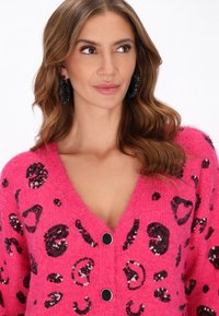 Rosa, flauschige Strickjacke mit einem Leopardenmuster aus schwarzen Pailletten, V-Ausschnitt und schwarzen Knöpfen auf der Vorderseite. Weicher Stoff und lockere Passform.