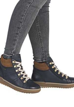 Baskets montantes en cuir bleu marine avec des accents marron, des garnitures dorées, des lacets blancs et une semelle en caoutchouc texturée. Fermeture éclair sur le côté.